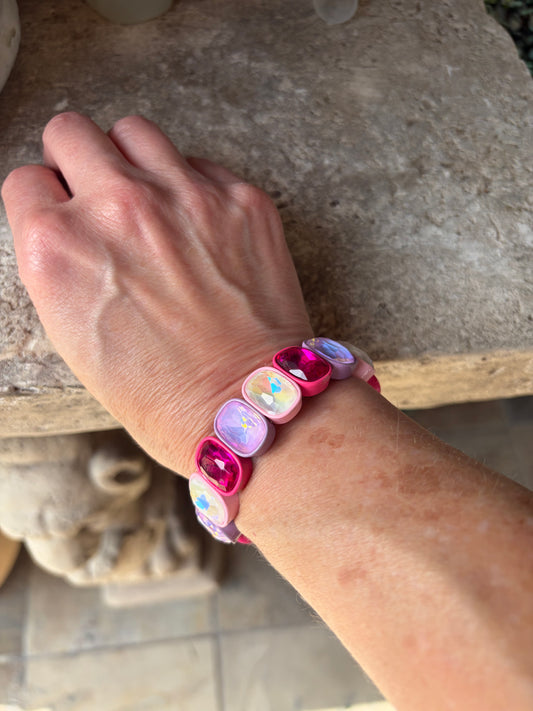 A close-up of a person's wrist wearing a beaded stretch bracelet with pink, purple, and iridescent square beads.