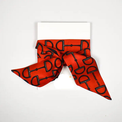 A red silk scarf with a black horsebit pattern