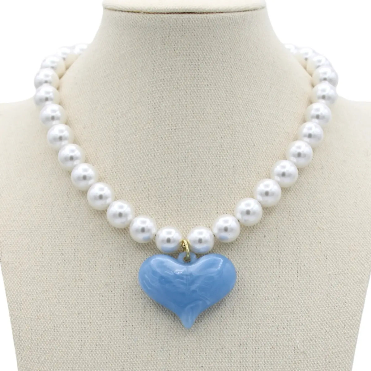 A pearl necklace that is 16v inches with a resin light blue heart pendant, displayed on a cream fabric mannequin bust.