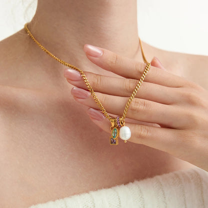 Gold necklace with small charm pendants featuring a pearl and gemstones, held by a hand.