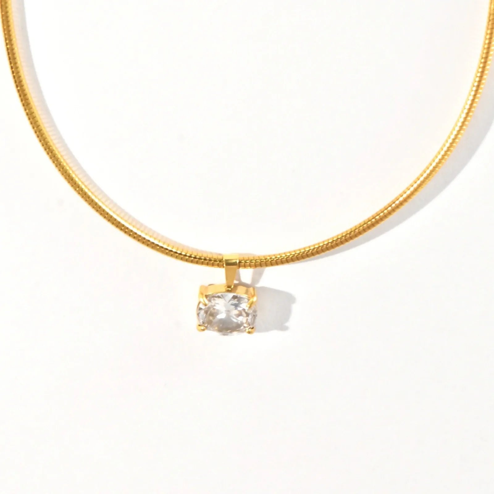 Gold necklace with a clear pendant on a white background