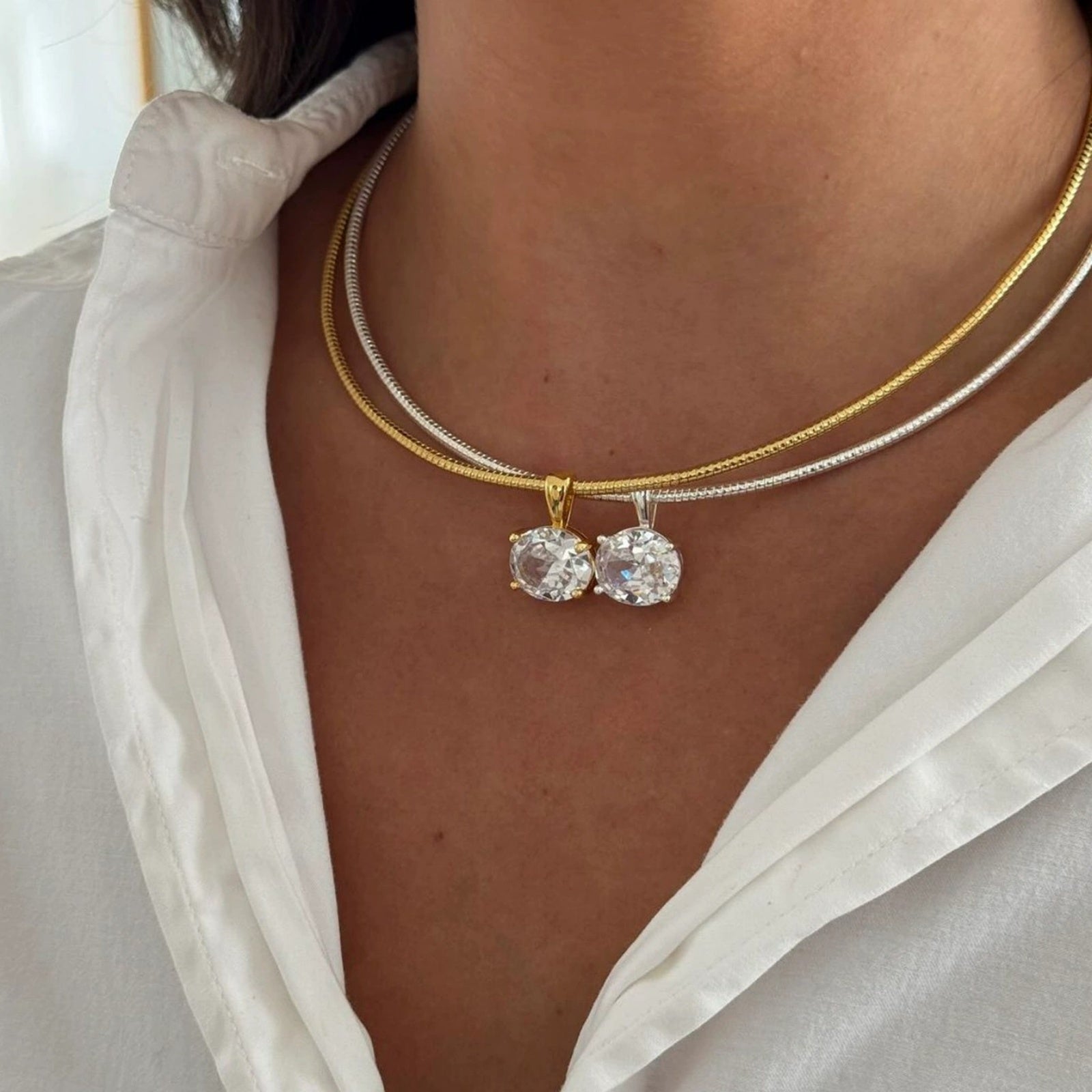 Close-up of a person wearing two gold necklaces with round pendants against a neutral background.
