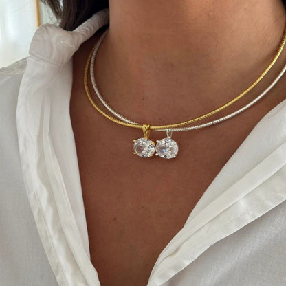 Close-up of a person wearing two gold necklaces with round pendants against a neutral background.
