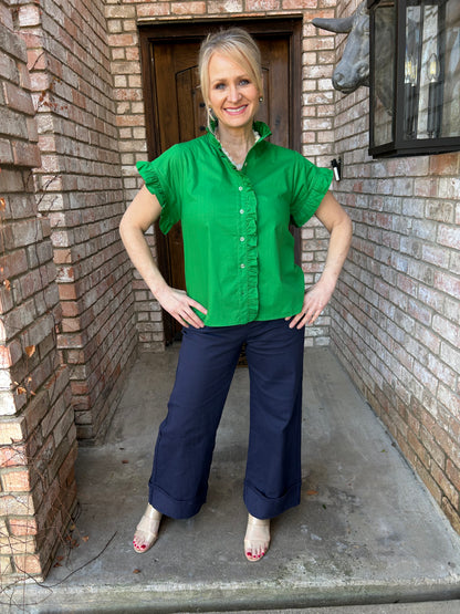 woman wearing a green short sleeve blouse, ruffled collar and sleeve, button down. Paired with navy blue cuffed pant