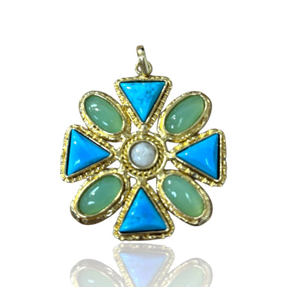 A gold-tone flower-shaped pendant featuring four bright blue triangular stones, four light green oval stones, and a central white round stone, shown on a white background with a soft reflection below.