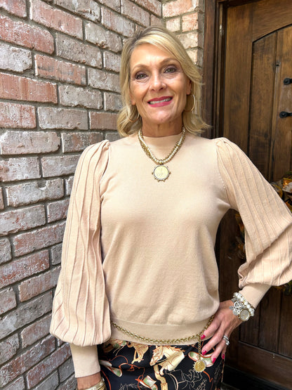 Woman in a beige sweater standing against a brick wall