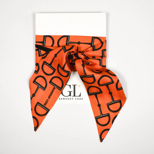 An orange silk scarf with a black horse bit pattern