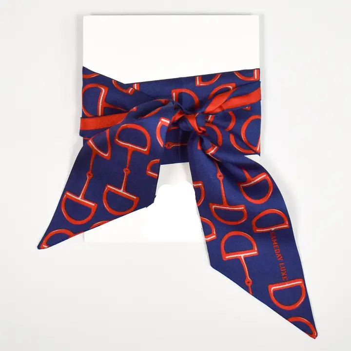 A navy blue silk scarf with a repeating red horse bit pattern 