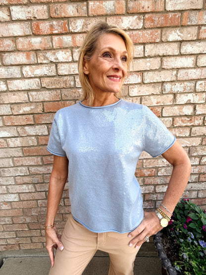 Woman wearing a light blue, short sleeve top with sequins. paired with a khaki pull on pants