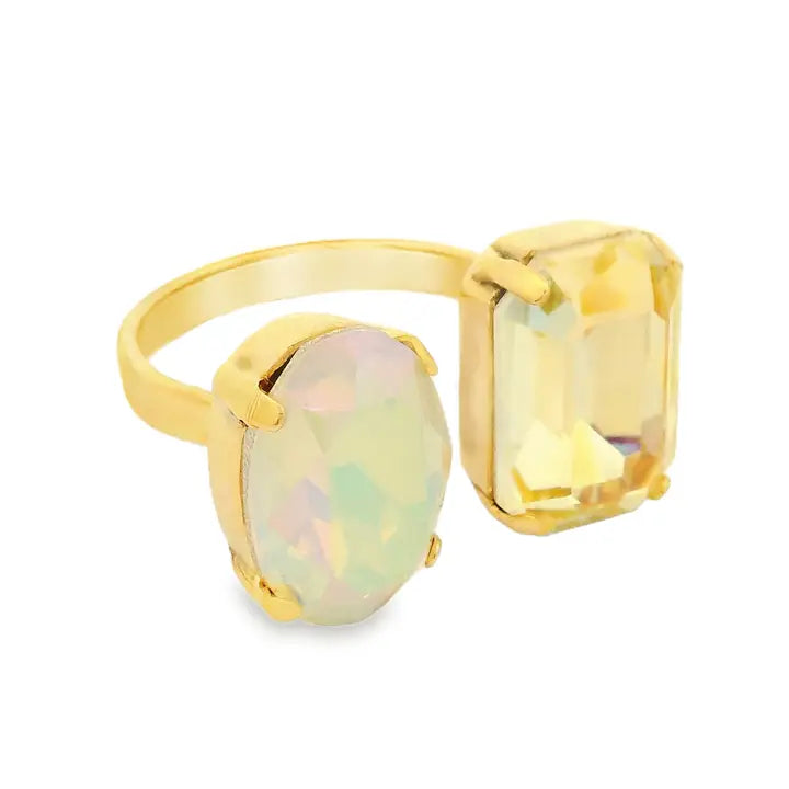 A gold ring featuring two large oval-cut stones, one with a pale iridescent opalescent sheen and the other a yellow emerald-cut stone, set against a plain white background.