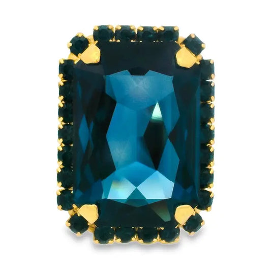 A rectangular emerald-cut blue gemstone ring with a gold halo setting and small accent stones, shown on a plain white background.